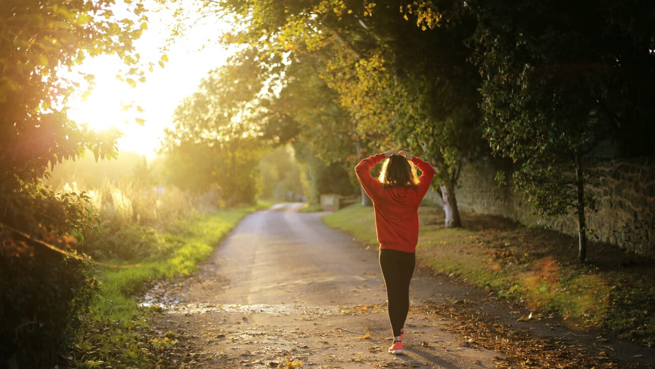 woman wearing red sneakers and sweat top, walking on a scenic country path with her hands on her head